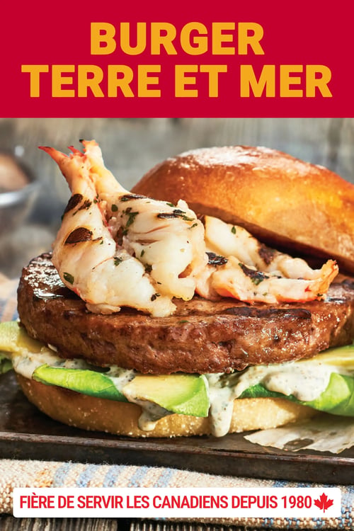 Les Aliments M&M - Page 24. La page présente une grande image d'un "Burger Terre et Mer". Le burger est composé d'une galette de viande, de tranches d'avocat, d'une sauce crémeuse et est garni de grosses crevettes grillées. Le tout est servi dans un pain brioché. Le fond de la page est rouge vif avec le titre "BURGER TERRE ET MER" en lettres jaunes. En bas de la page, sur une bande blanche, on peut lire "FIÈRE DE SERVIR LES CANADIENS DEPUIS 1980" avec une feuille d'érable rouge.