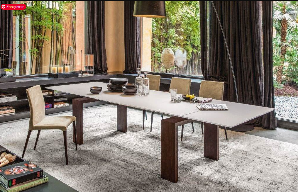 Salle à manger élégante avec une grande table extensible au design moderne, entourée de chaises en velours, dans un espace lumineux avec vue sur un jardin verdoyant de chez Maison Tessier