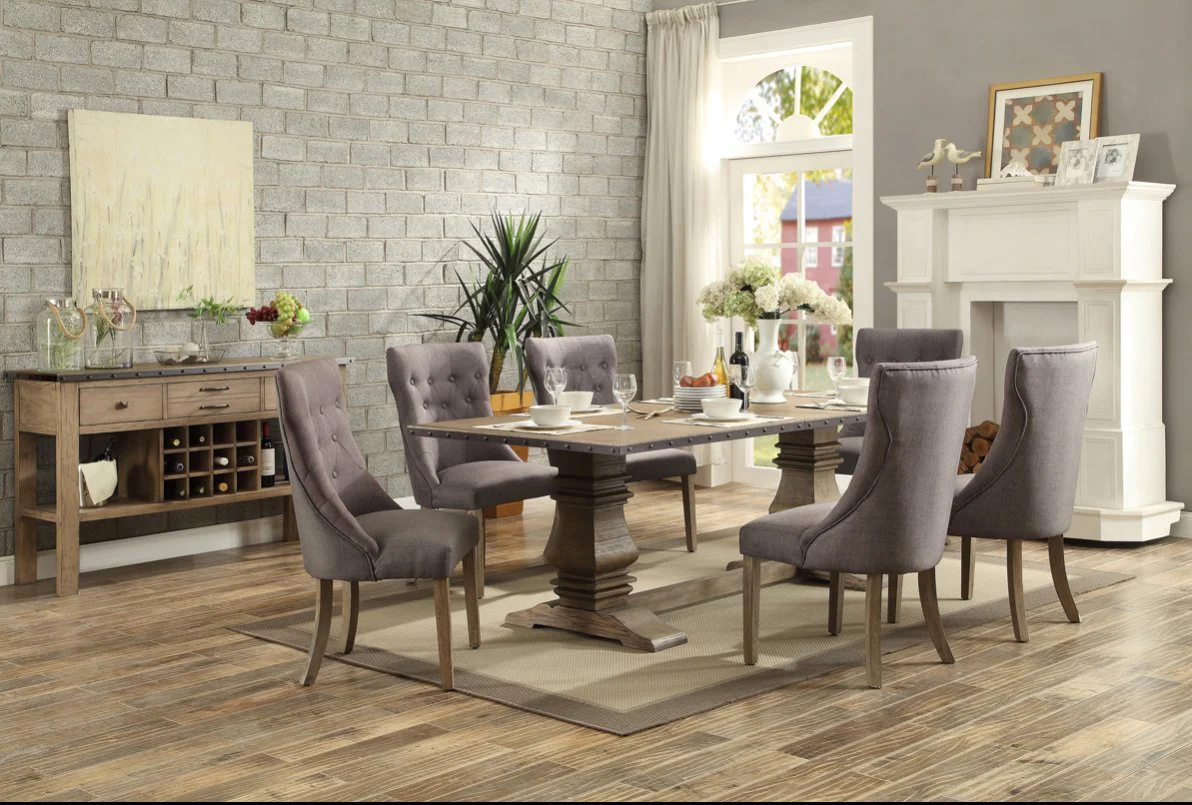 Salle à manger élégante au style rustique chic avec une grande table en bois massif, des chaises capitonnées grises, un buffet avec rangement pour bouteilles et une cheminée blanche décorative de chez Meubles Casa