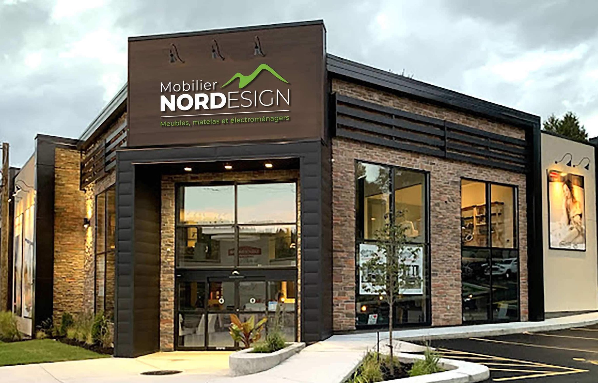 Façade du magasin Mobilier NORDESIGN à Sainte-Agathe-des-Monts, spécialiste en meubles, matelas et électroménagers, avec une architecture moderne en briques et un éclairage chaleureux.