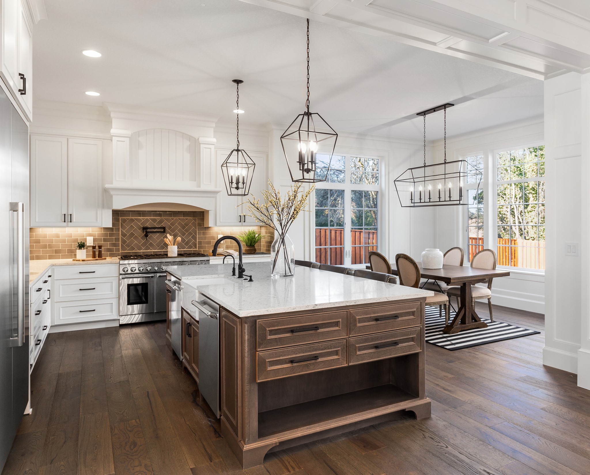 Cuisine haut de gamme moderne avec îlot central en bois foncé, armoires blanches et luminaires suspendus – réalisation par RenoVilla